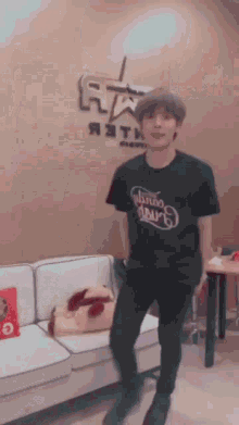 a young man in a black t-shirt is standing in front of a couch .