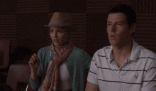 a woman wearing a hat and a scarf stands next to a man wearing a striped shirt