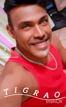 a man wearing a red tank top and a silver chain smiles