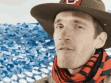 a man wearing a cowboy hat and a scarf has a u on his hat