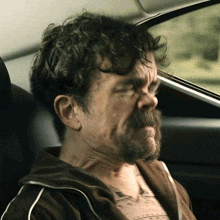 a man with a beard and a tattoo on his chest is sitting in the back seat of a car