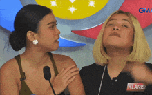 two women are talking in front of a sign that says klaris