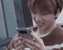 a young man is holding a cell phone in his hand and smiling .