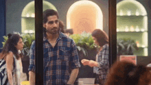 a man in a plaid shirt is standing in front of a window with a woman standing behind him .