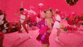 a woman in a pink dress is dancing in front of a pink background with balloons and candies