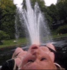 a woman is laying in front of a fountain with water coming out of her mouth
