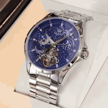 a silver and blue olevs watch sits on a white box