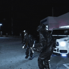a man in a hooded jacket stands in front of a white suv at night