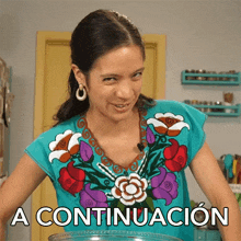 a woman wearing a blue shirt with flowers on it stands in front of a sign that reads a continuacion