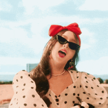 a woman wearing a polka dot top and sunglasses has a red bow on her head