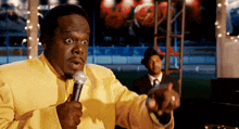 a man in a yellow suit is speaking into a microphone and pointing