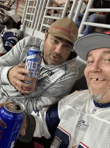 two men sitting in a stadium holding cans of miller lite beer