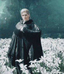 a man standing in a field of white flowers wearing a black cape