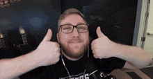 a man wearing glasses giving a thumbs up in front of a microphone