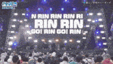a crowd of people watching a concert with the words rin rin go on the screen