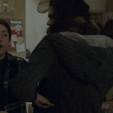 a woman with a scarf around her neck stands next to another woman in a kitchen