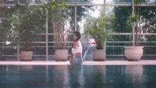 a woman is standing next to a swimming pool surrounded by potted plants