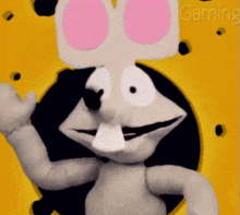 a stuffed animal with pink eyes is waving in front of a yellow background that says gaming