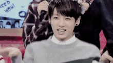 a young man wearing a gray sweater and a flower crown is smiling .