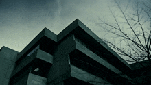 a building with a tree in the foreground and a cloudy sky in the background