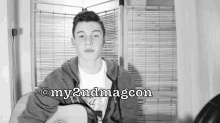 a black and white photo of a young man playing a guitar with the words @my2ndmagcon below him