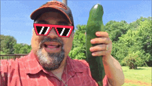 a man wearing sunglasses and a hat is holding a cucumber
