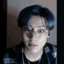 a man with blue hair and glasses is wearing a plaid shirt and a necklace .