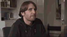 a man with a beard is wearing a black hoodie with the letter u on the front