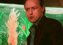 a man in a plaid jacket and tie is standing in front of an aquarium with corals .