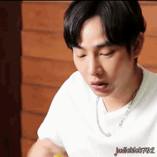a young man wearing a white shirt and a necklace with the name judikleh702 on the bottom