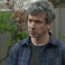 a man with gray hair is wearing a blue plaid shirt and a black shirt