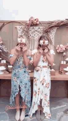 two women in floral dresses are posing for a picture with their eyes covered .