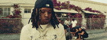 a man with dreadlocks is wearing a black hat and a white shirt .