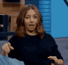 a woman in a black sweater is sitting on a couch with her mouth open .