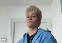 a young man wearing a blue hoodie and a black shirt is standing in a room .