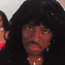 a man with long hair and a mustache is wearing a wig and a necklace .