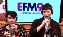 two men wearing headphones are drinking water through a straw in front of a screen .
