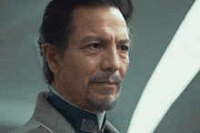 a man with a beard is wearing a collar with a silver triangle on it