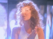 a woman with curly hair is wearing a white tank top and dancing in a club .