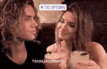 a man and a woman are holding drinks in front of a sign that reads tao uptown