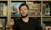 a man smoking a cigarette in front of a shelf full of board games including cuphead