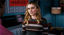 a woman in a striped sweater stands in front of a sign that says work harder