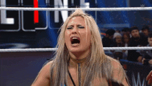 a woman is screaming in a wrestling ring with a crowd behind her