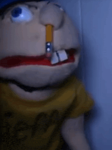 a puppet with a cigarette in his mouth is wearing a yellow shirt and a blue hat .