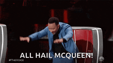 a man in a blue suit is sitting in a chair with his arms outstretched and says all hail mcqueen .