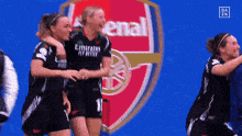 a group of women hugging in front of a arsenal logo