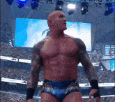 a shirtless wrestler is standing in front of a crowd in a stadium with a sign that says jh on it
