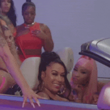 a group of women are sitting in a convertible car and one of them is reaching out to touch another woman 's hand .