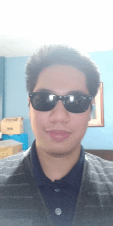 a man wearing sunglasses looks at the camera with boxes in the background