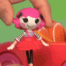 a doll with pink hair and a striped shirt is being held by a person